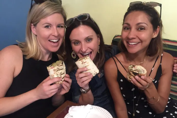 Three women smiling and holding wraps in a casual setting.