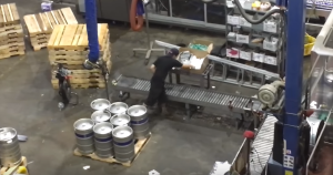 a warehouse with a conveyer belt and several kegs of beer