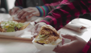 a sanwich being held by a man with another in the background