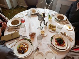 a table set with cloth linens and place settings of soup and fancy meals