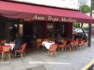 a group of people sitting at a table with a red umbrella outside of a restaurant