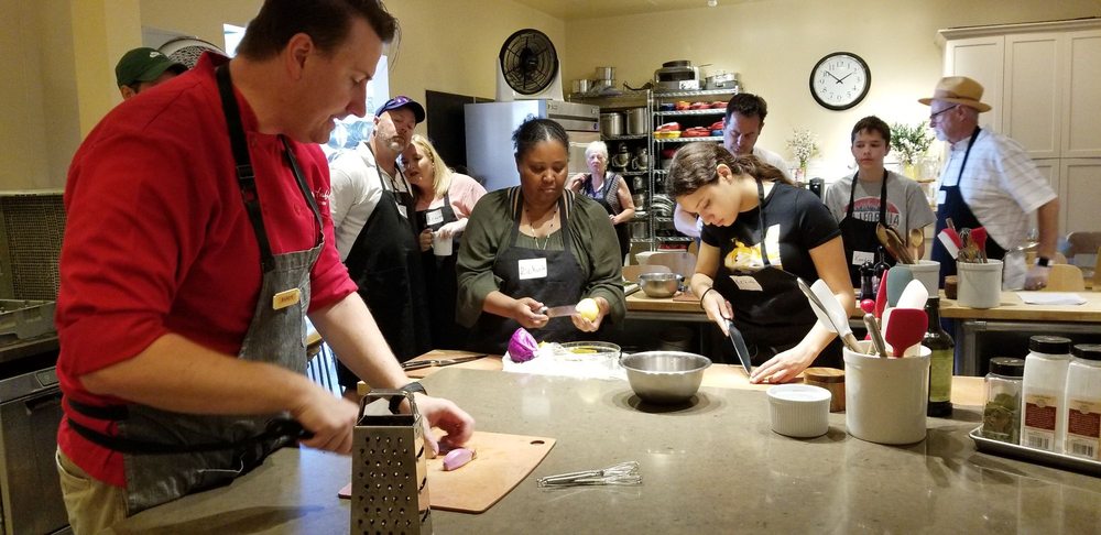 a group of people standing around a table cooking together