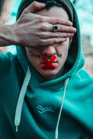 a close up of a person covering their eyes with mouth taped and words "don't lie"