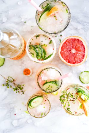 cocktail glasses with herbs, citrus, cucumber, and straws
