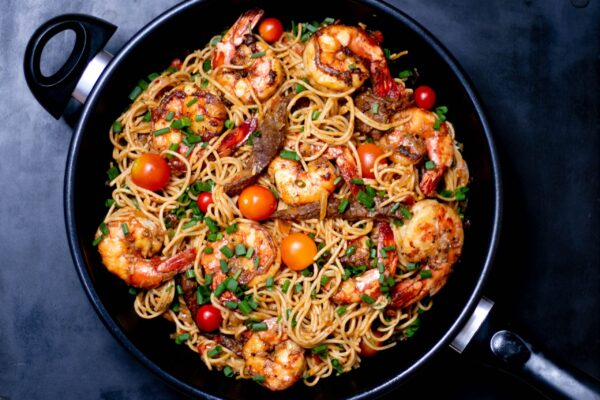 a skillet with pasta, shrimp and tomatoes