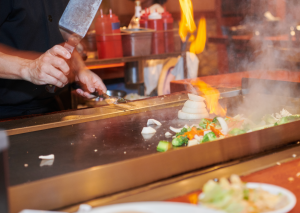 The arms of a hibachi chef preparing food on the flat top