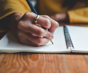 arm with yellow sleeve and gold wring writing in a spiral notebook