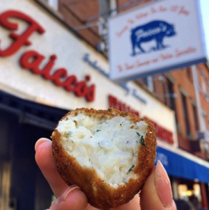 a hand holding a half eaten arancini risotto ball