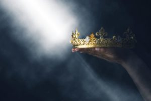 a close up of a gold crown help up by a woman's hands in a spotlight