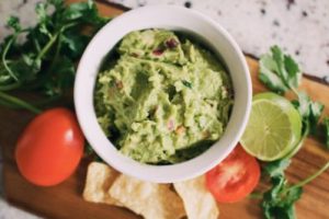 guacamole in a small bowl with fresh ingredients beside it