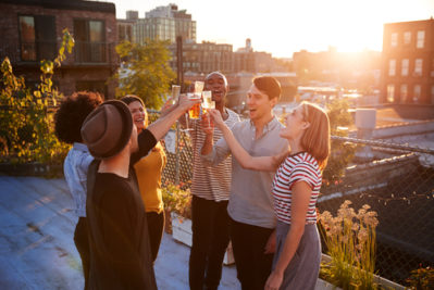 Friends,Make,A,Toast,At,A,Rooftop,Party,,Backlit,By a group of people standing on a rooftop with drinks at sunset