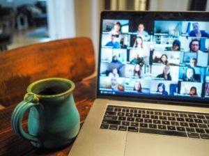 a laptop computer sitting on top of a table during a video call with many people. also a green mug on the table
