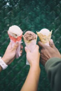 three hands holding out different flavors of ice cream cones