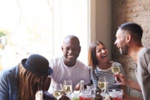 A group of friends laughing over food and drinks at a restaurant with exposed brick