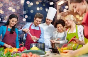 A group of people wearing colorful aprons standing with a chef taking a cooking class