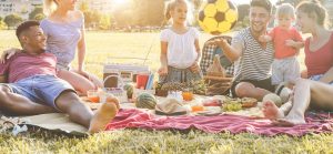 Young parents having fun with their children in summer time eating, laughing and playing together at the park