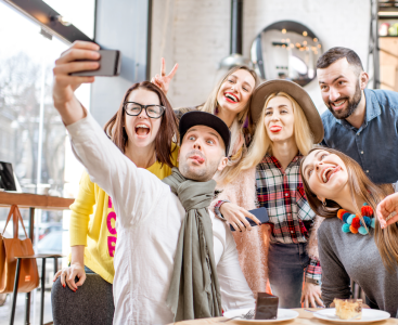 Young friends dressed casually having fun making self portrait together in the cafe