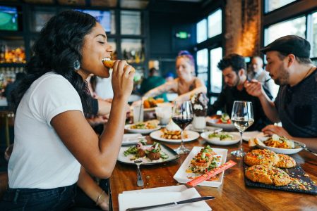 a group of people sitting at a table eating, with the main focus on a young girl eating a huge delicious cookie