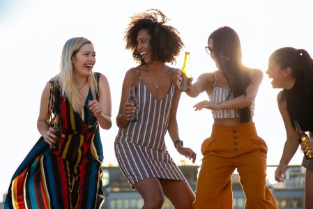 Laughing young diverse girlfriends dancing and drinking beer during event