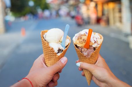 hands holding ice cream cones with bright colored spoons