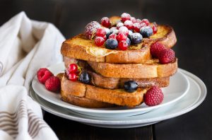 Traditional French toast with berries: blueberries, currant, raspberries and icing sugar for perfect sweet breakfast. Delicious dessert background.