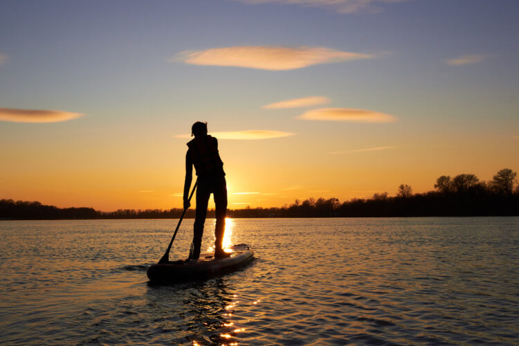 a man with long hair and a sunset over a body of water