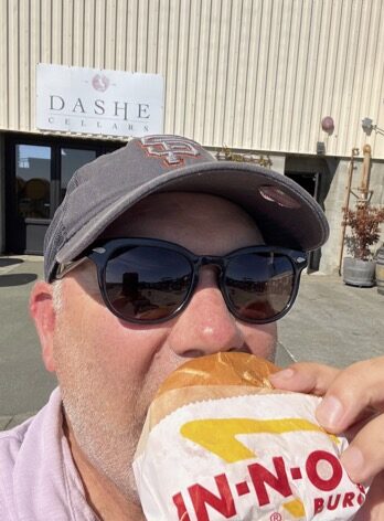 a man wearing a hat and sunglasses eating a hot dog