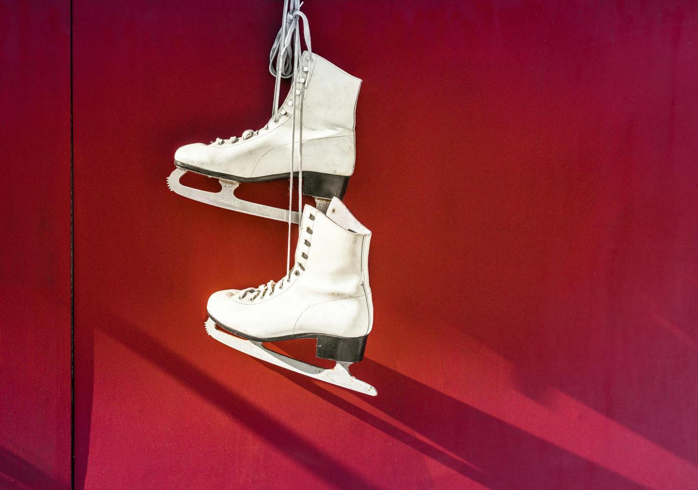 White ice skates hanging up against a red wall