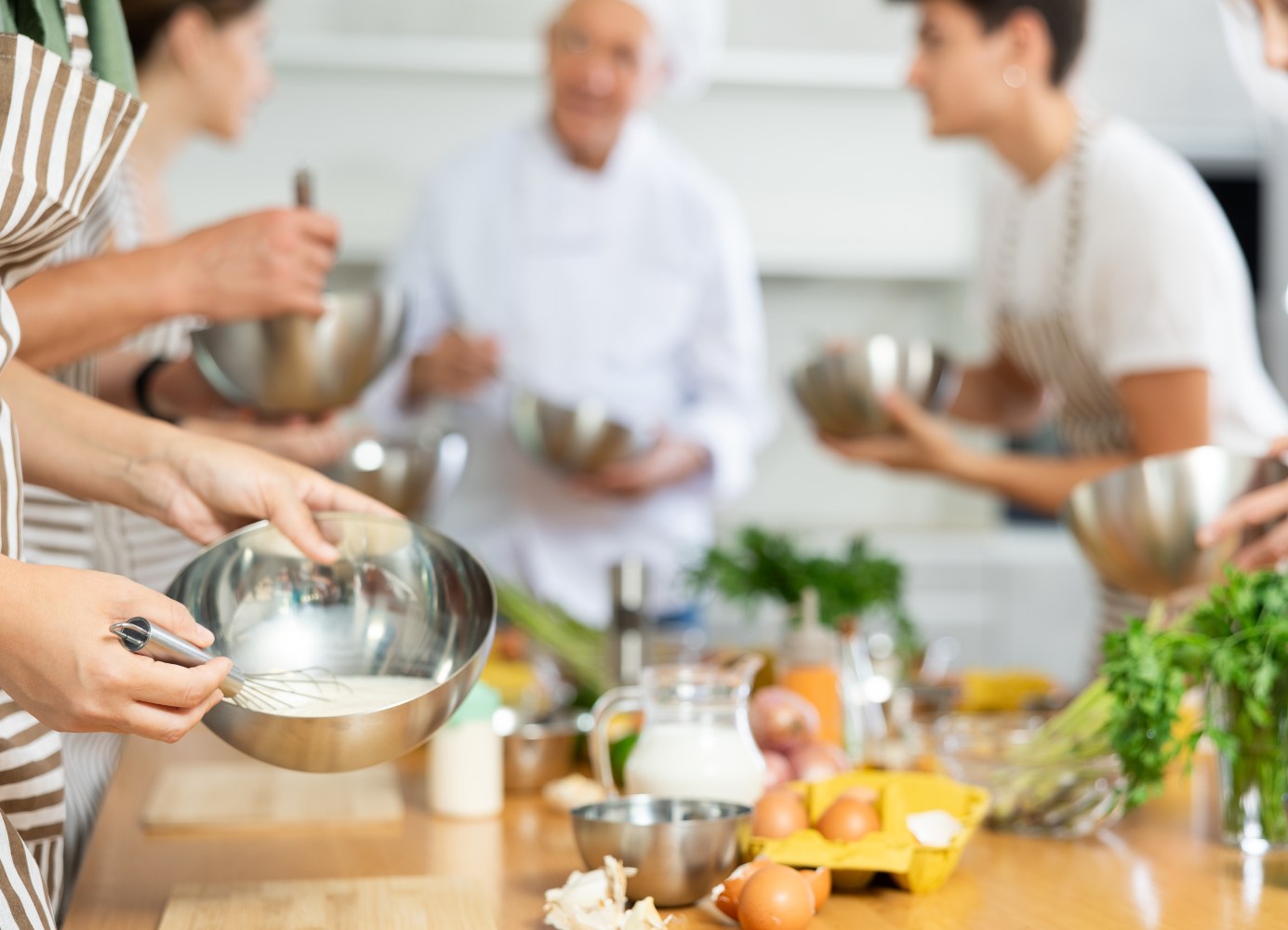 A group of people wearing aprons at a cooking class while whisking eggs