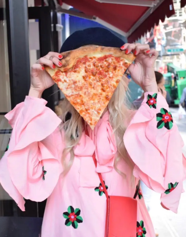 a girl holding a large slice of pizza in front of her face