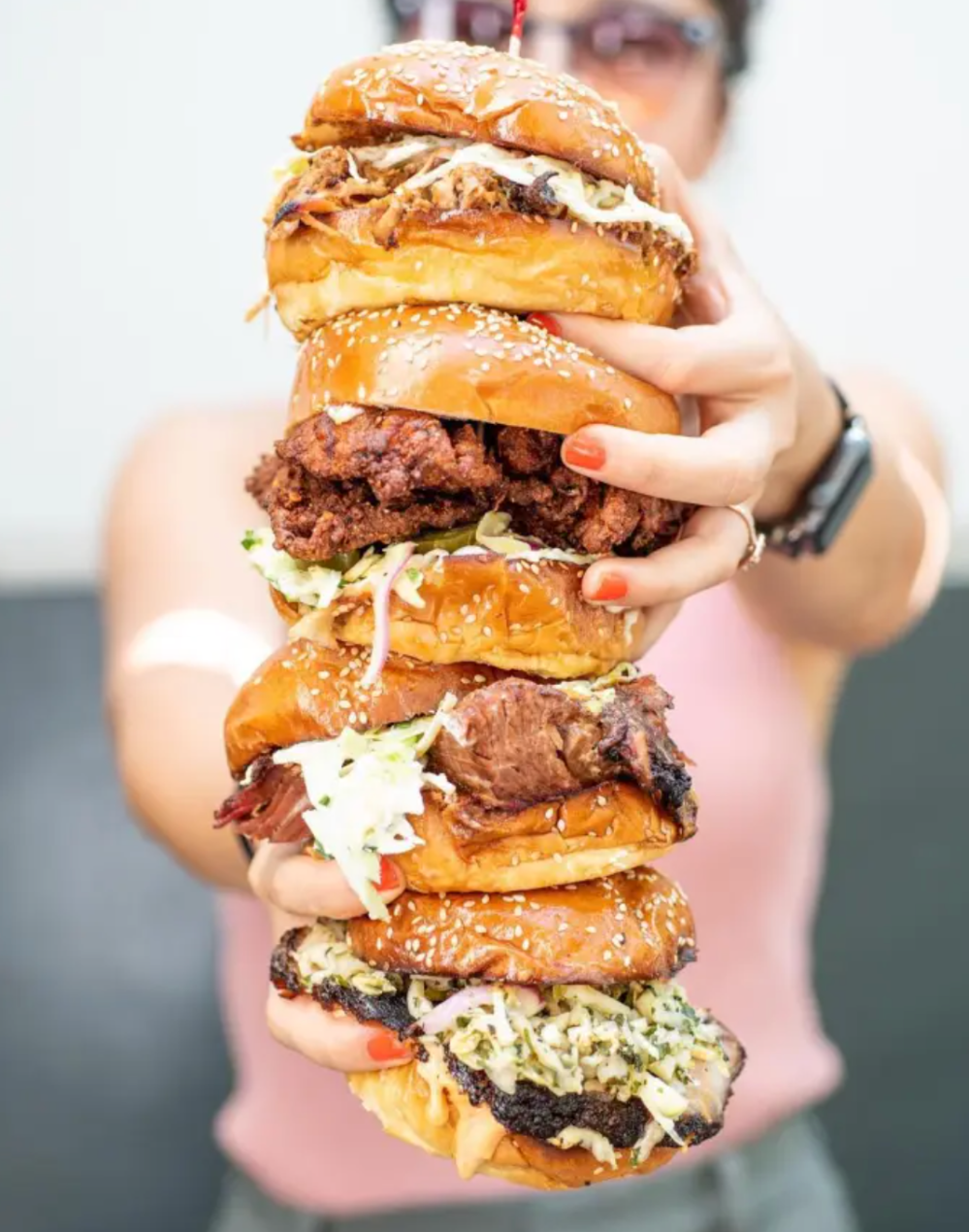 a close up of a person holding four sandwiches stacked