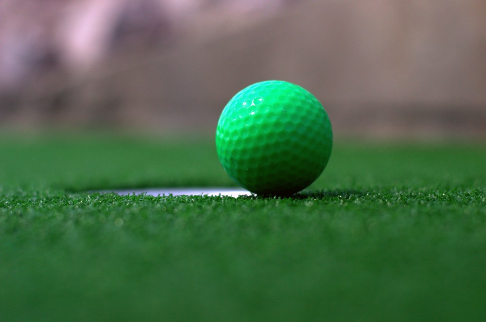 a green ball on a course right about to go in the golf hole