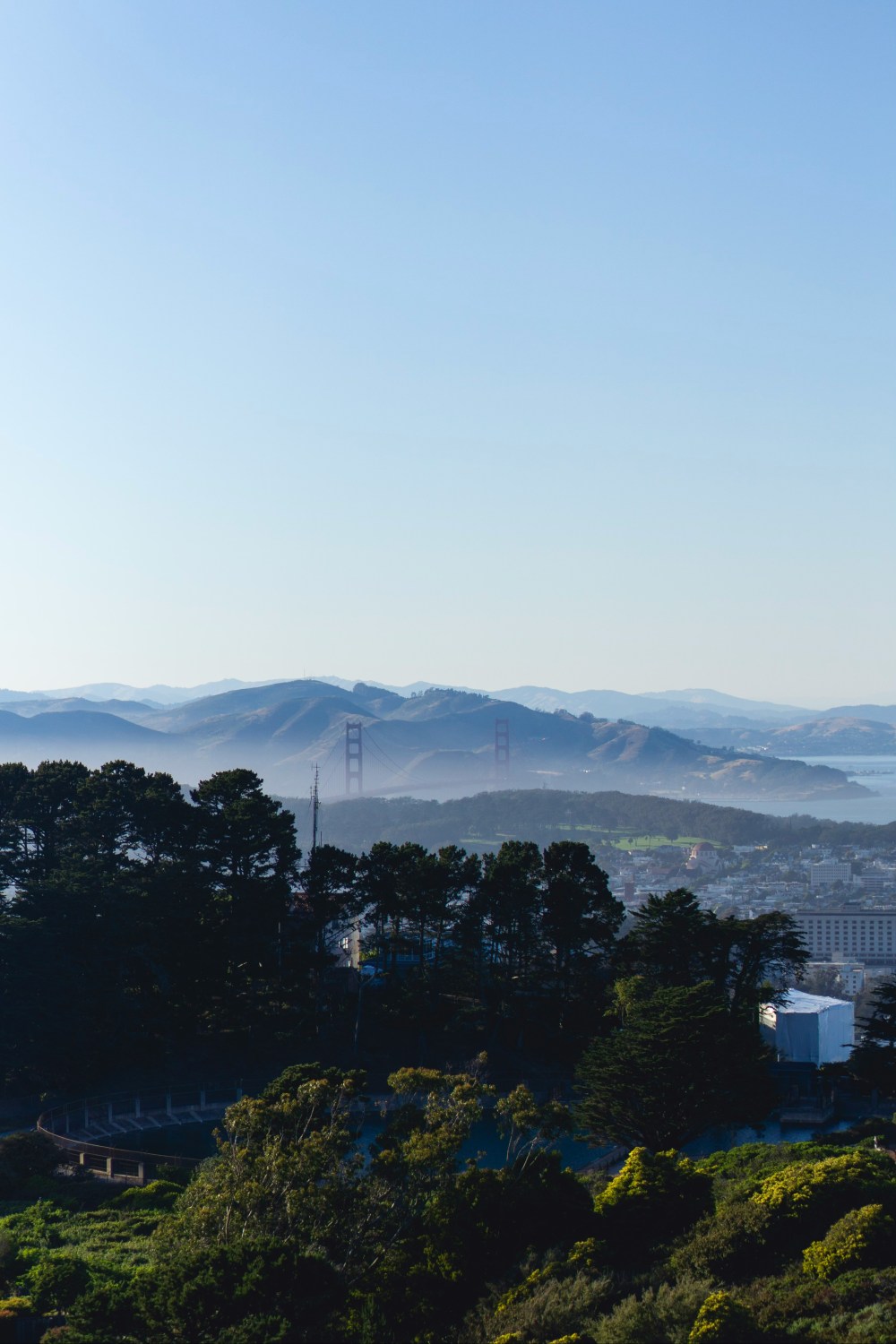 Scenic view of hills, trees, and a bridge under a clear blue sky.