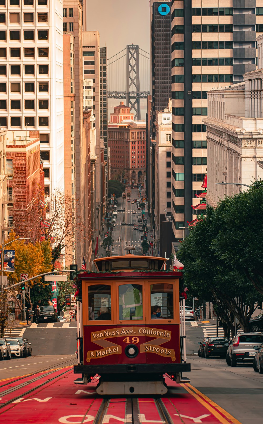 Red cable car on city street with bridge in background.
