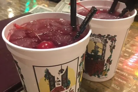 Two white cups with cherry slush drinks and black straws on a bar counter.