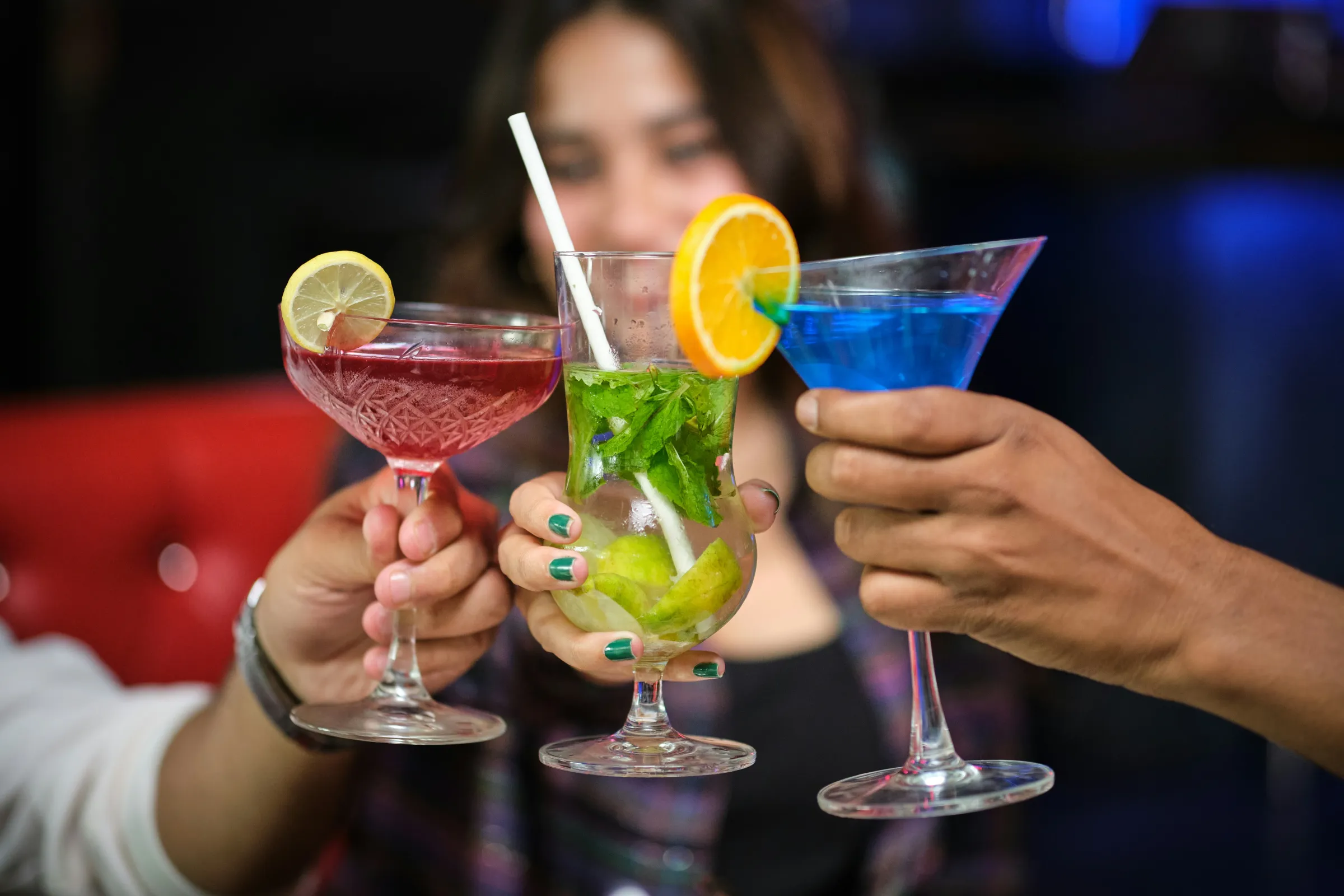 Cocktail Tour 9 Three people toasting with colorful cocktails, including blue, red, and green drinks.
