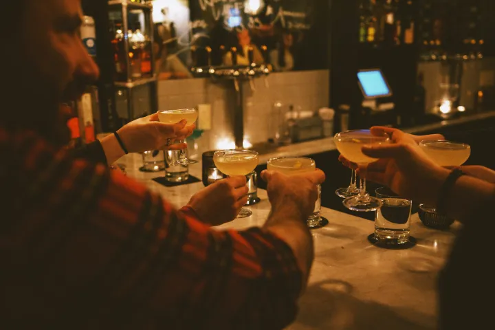 People toasting with cocktails at a dimly lit bar.