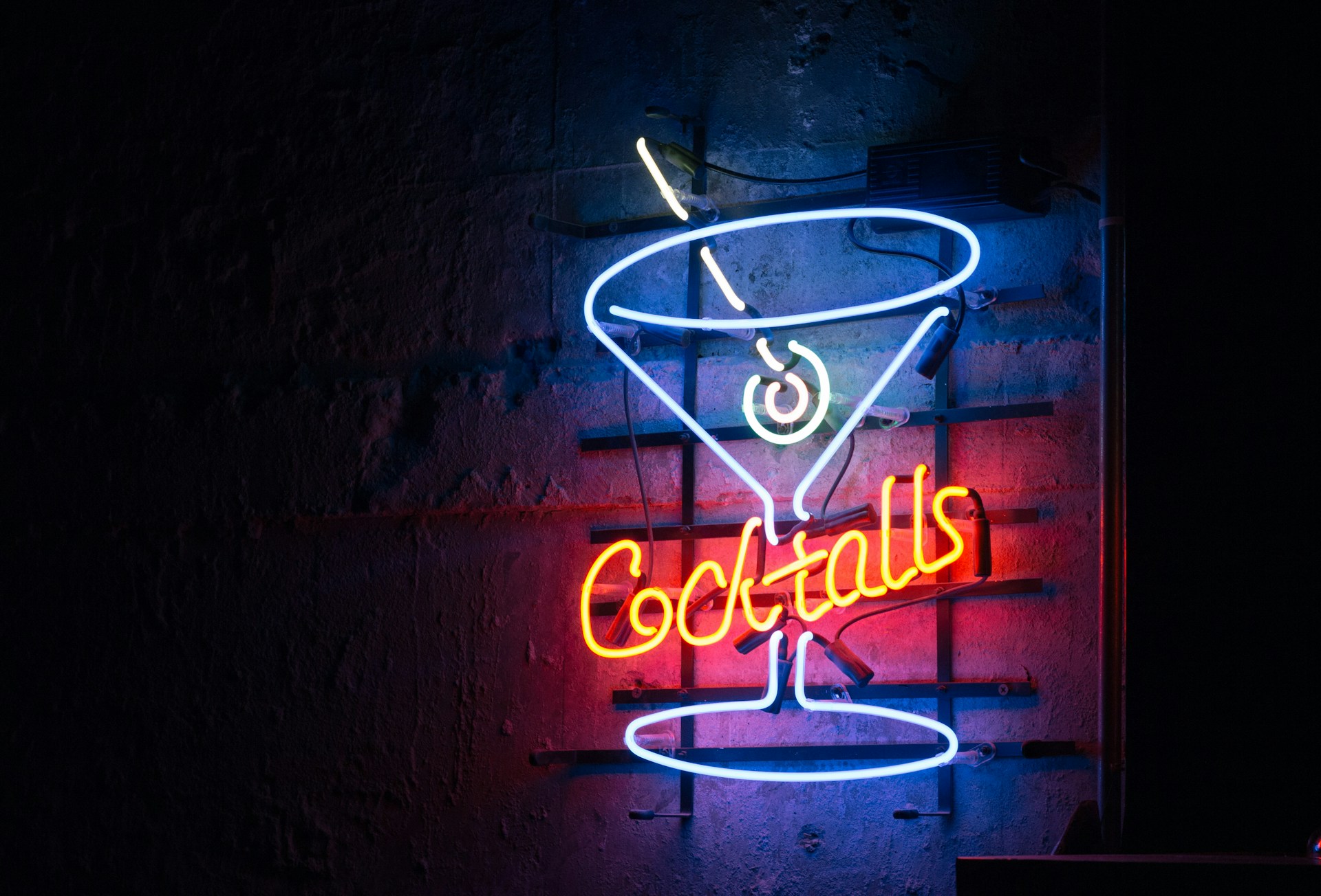 cocktails sign Neon sign of a cocktail glass with an olive and the word 'cocktails' on a dark wall.