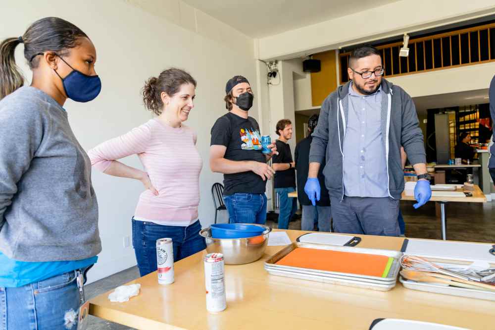 People standing around a table with cooking trays and utensils in a bright room.
