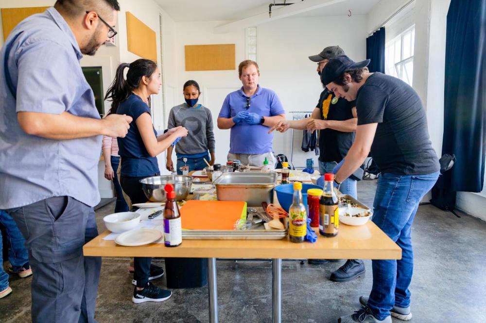Group of people gathered around a table with cooking ingredients and utensils.