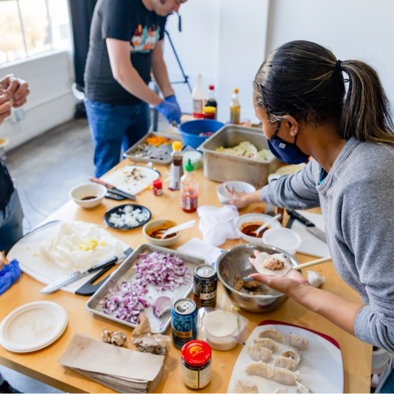 Group of people preparing dumplings at a table with various ingredients.