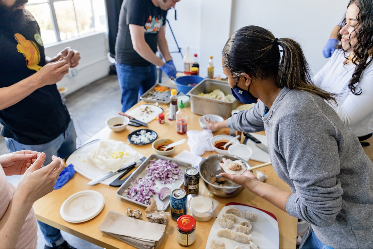 Group of people preparing dumplings at a table with various ingredients.