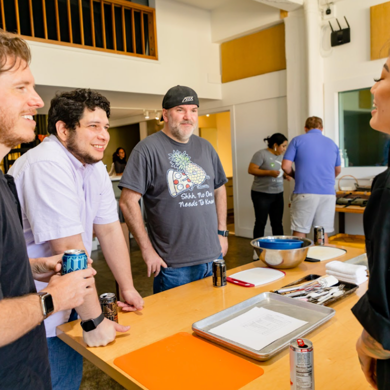 Four people chatting around a table with cooking utensils in a casual setting.