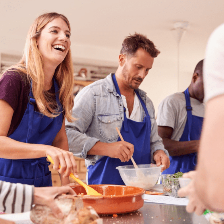 Group of people in blue aprons cooking together in a kitchen.