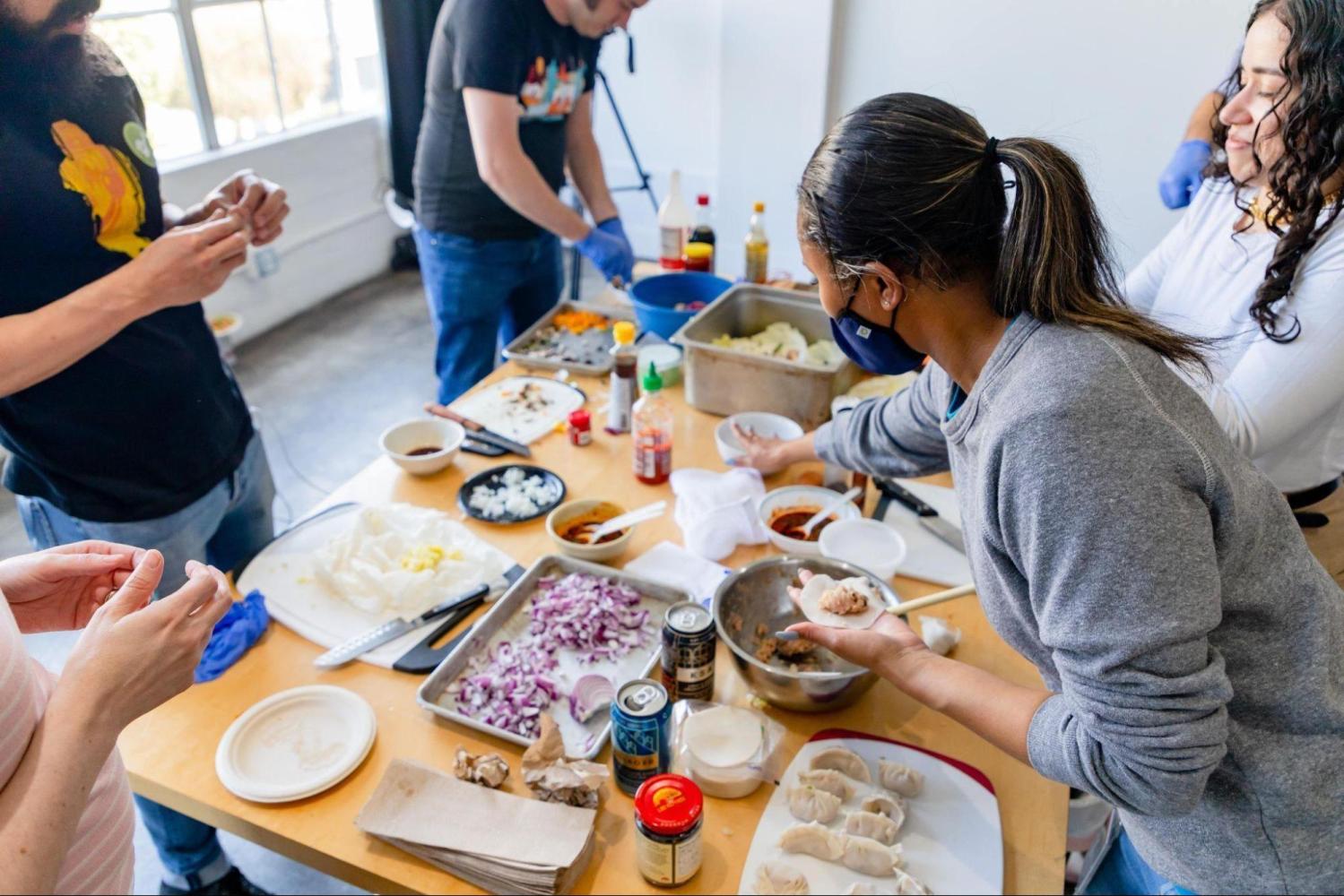 People preparing food around a table with ingredients and utensils.