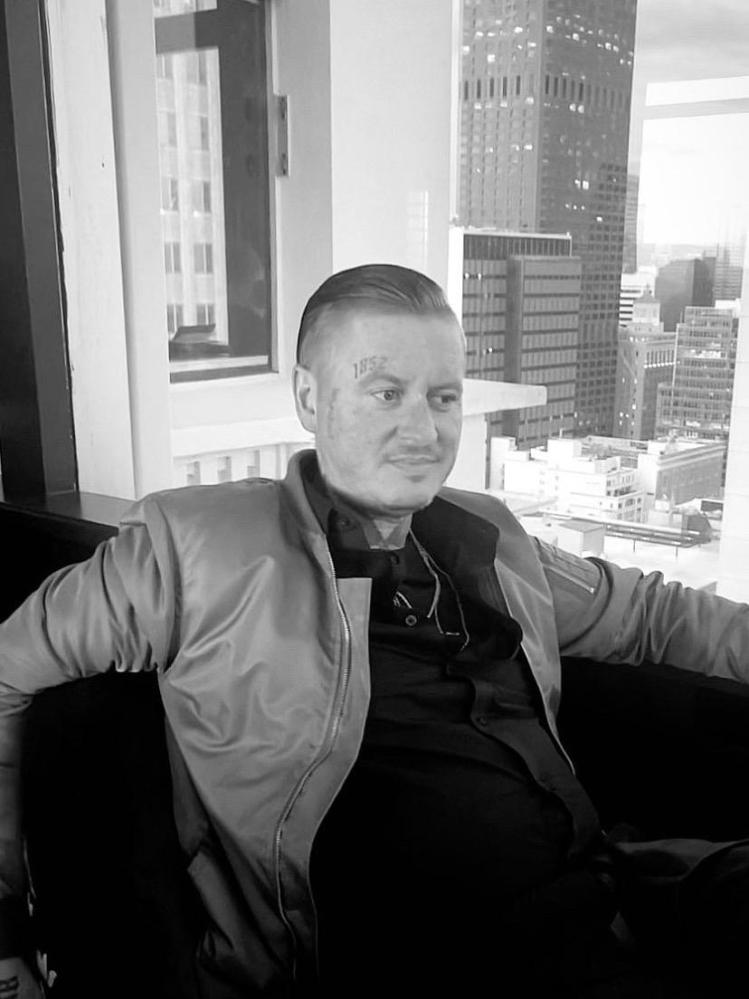 Man sitting by window in an urban setting, wearing a jacket and looking outside.