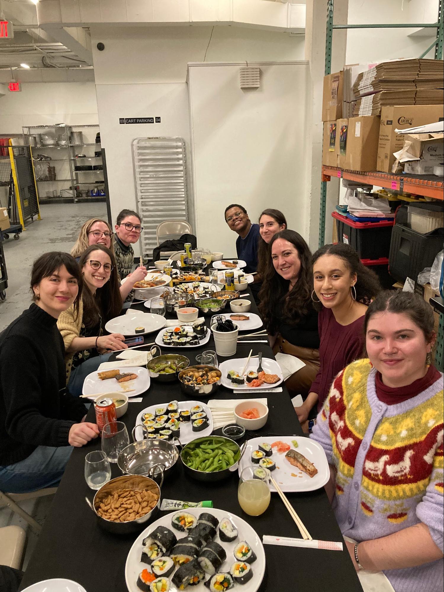 Group of people enjoying sushi at a long table in a storage room setting.