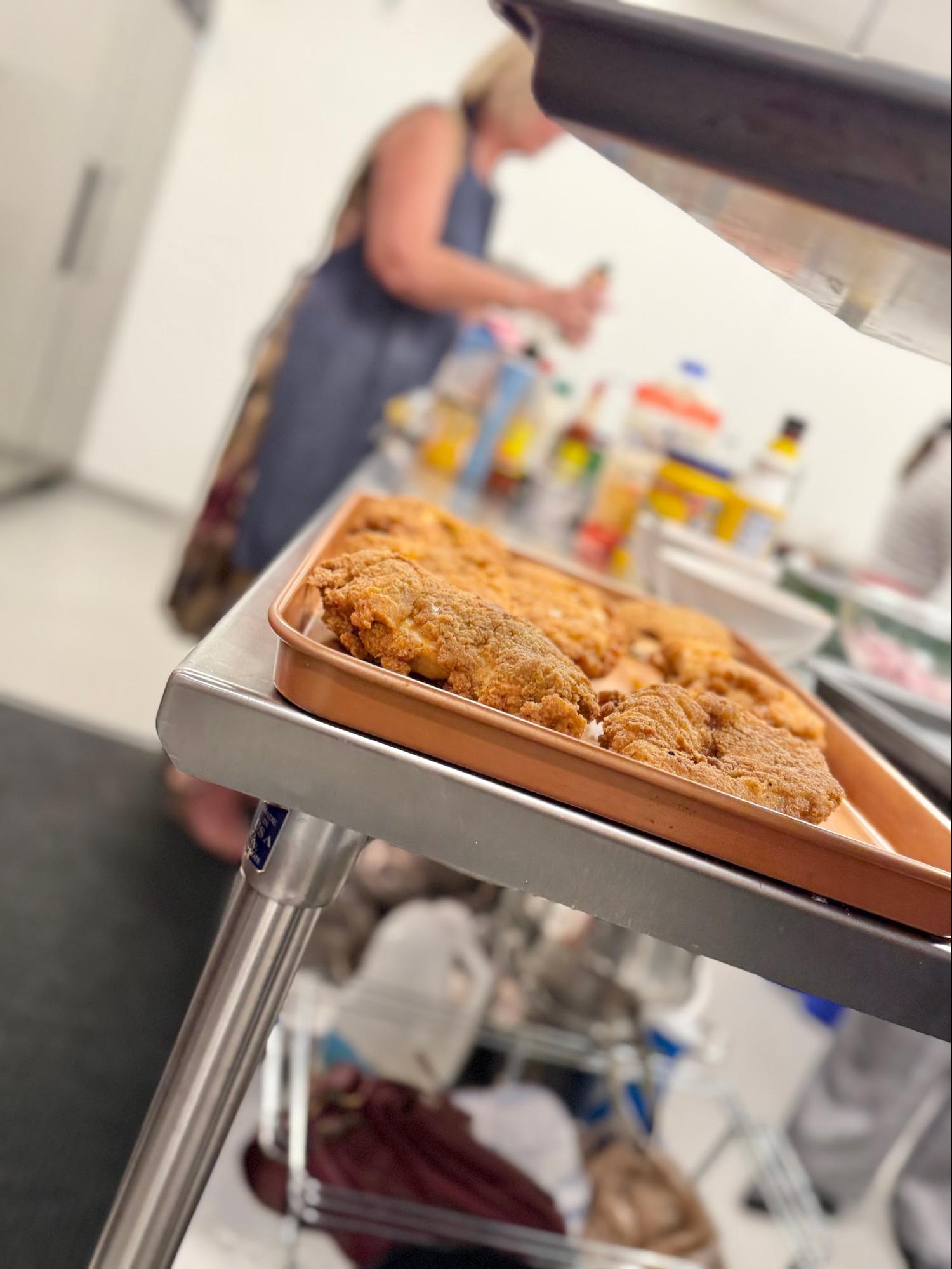 Tray of fried chicken with a blurry person in the background in a kitchen setting.