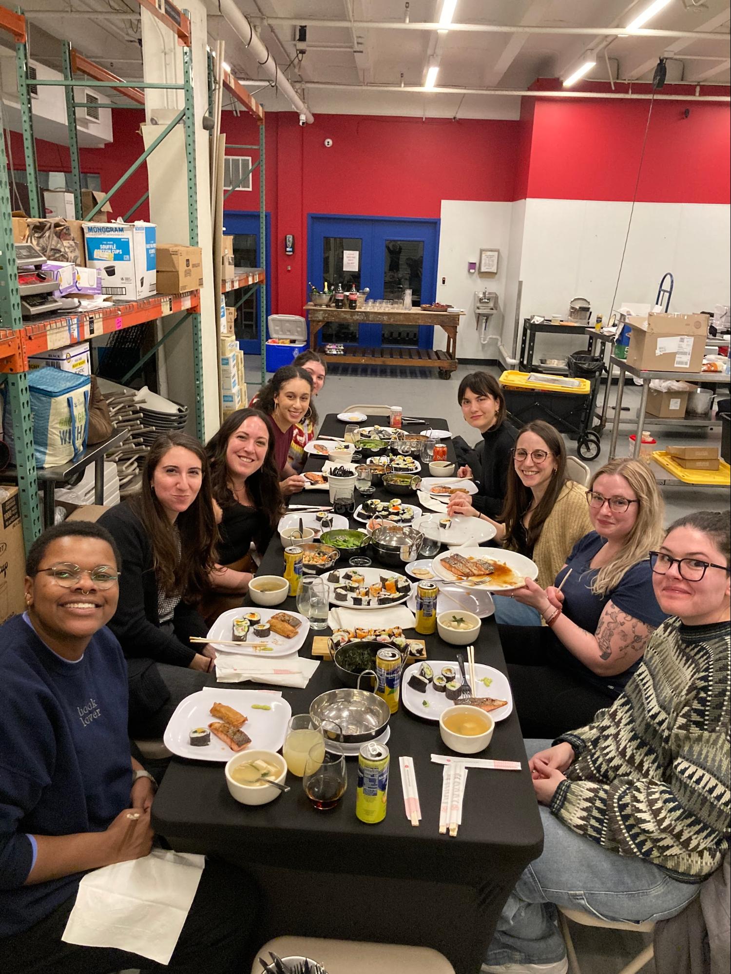 Group of people sitting around a table with sushi in a warehouse setting.