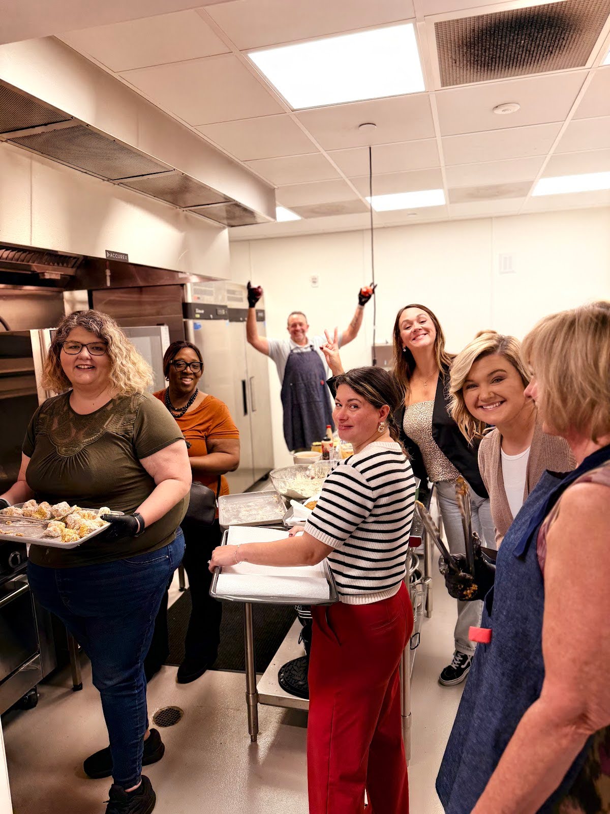 People in a kitchen preparing food, smiling and posing for a group photo.